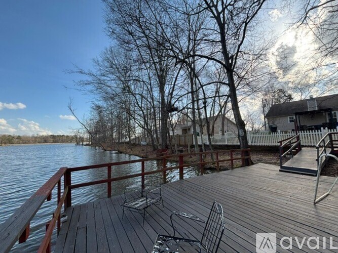 A wooden deck overlooks a body of water with trees and houses in the background.