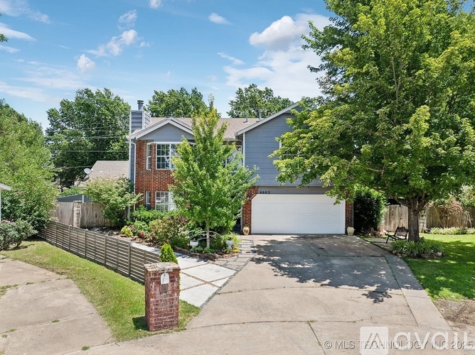 A house with a garage is surrounded by a fence and trees.