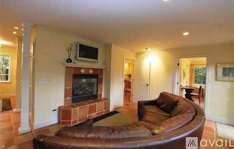 A living room with a brown leather couch and a brick fireplace.