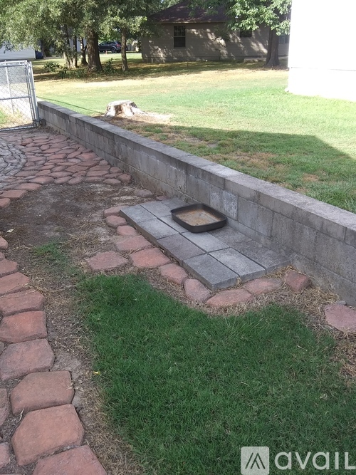 A stone pathway leads to a small square concrete structure in the middle of a grassy area.
