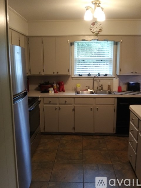 A kitchen with a refrigerator on the left and cabinets below a window.