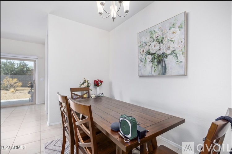 A dining room with a wooden table and chairs, a vase with flowers, and a painting on the wall.