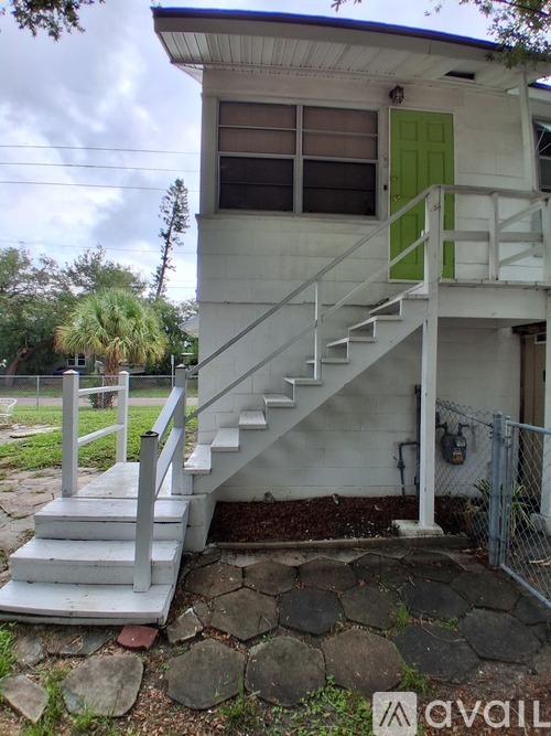 A white house with a green door and a staircase leading to the second floor.