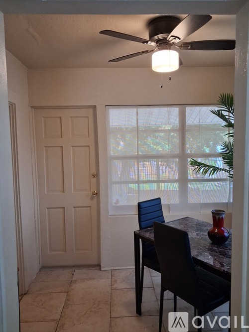 A room with a ceiling fan and a table with a blue chair and a red vase.