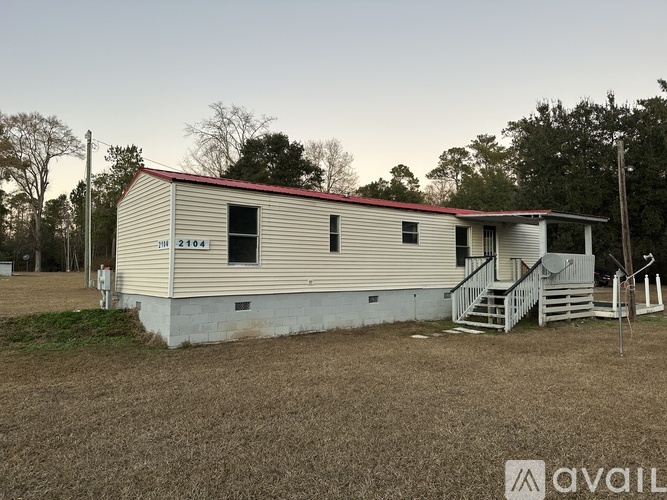 A mobile home with a red roof is situated in a grassy area with trees in the background.