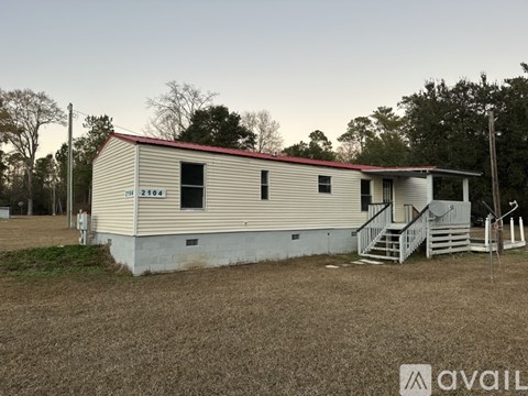 A mobile home with a red roof is situated in a grassy area with trees in the background.