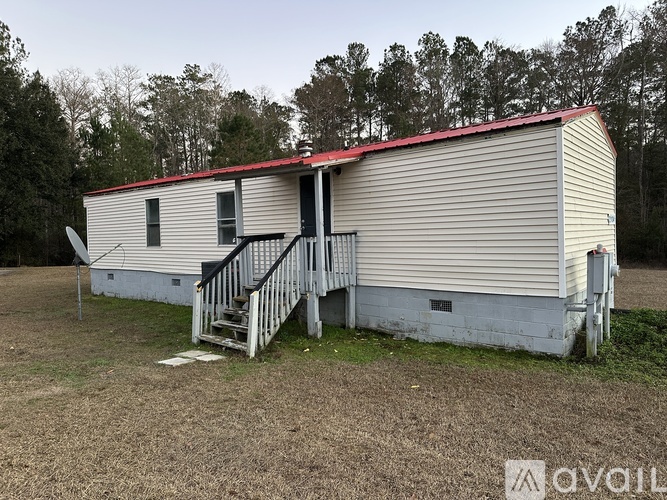 A mobile home with a red roof is situated in a grassy area with trees in the background.