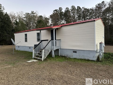 A mobile home with a red roof is situated in a grassy area with trees in the background.