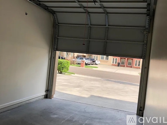 A view from inside a garage looking out to a parking lot and a building.