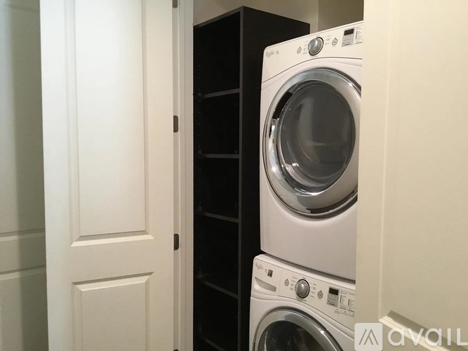 A white washing machine is in a small space between a door and a cabinet.