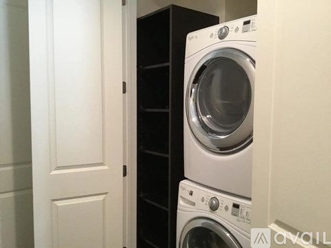 A white washing machine is in a small space between a door and a cabinet.