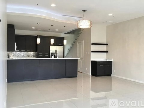 A modern kitchen with black cabinets and a staircase in the background.