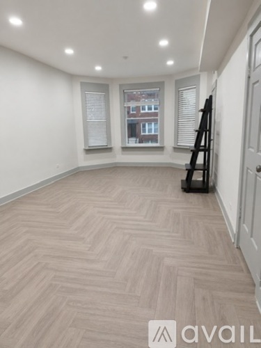 A room with a herringbone patterned floor and a window showing a building outside.