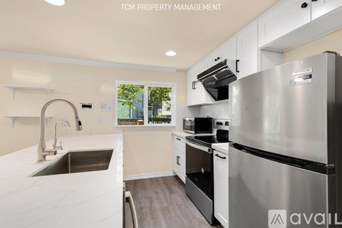 A modern kitchen with a stainless steel refrigerator and a window showing a view of trees.