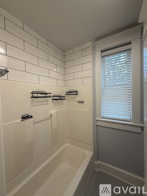 A bathroom with a white tiled shower area and a window with blinds.