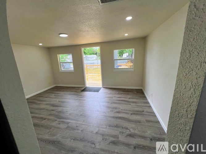A room with wooden flooring and two windows overlooking a street.