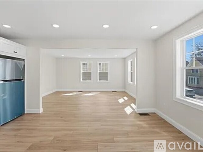 A spacious empty room with wooden flooring and a large window.