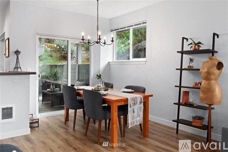 A dining room with a wooden table and chairs, a chandelier, and a shelf with decorative items.