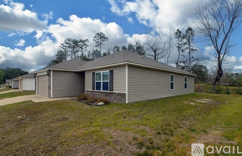 A house with a brown roof and a grey siding is surrounded by grass and trees.