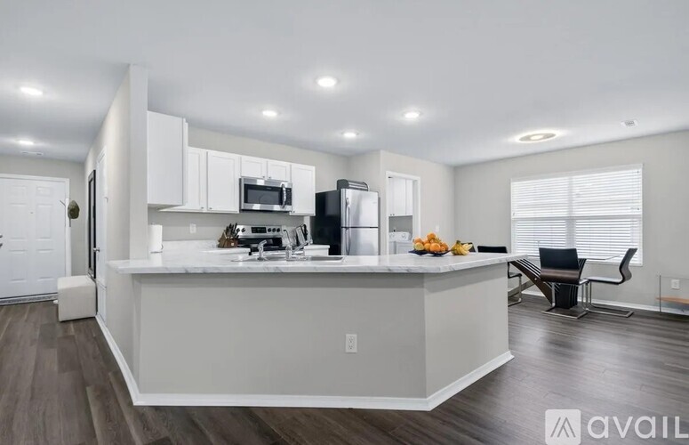 A kitchen with white cabinets and a white island with a refrigerator, microwave, and a bowl of fruit on top.