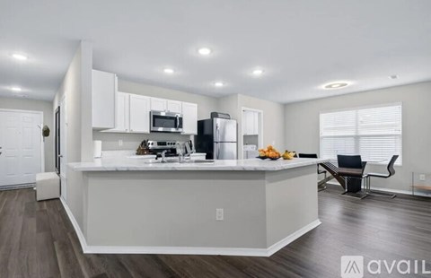 A kitchen with white cabinets and a white island with a refrigerator, microwave, and a bowl of fruit on top.