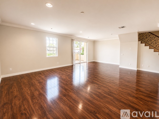 A spacious room with wooden floors and a staircase on the right side.