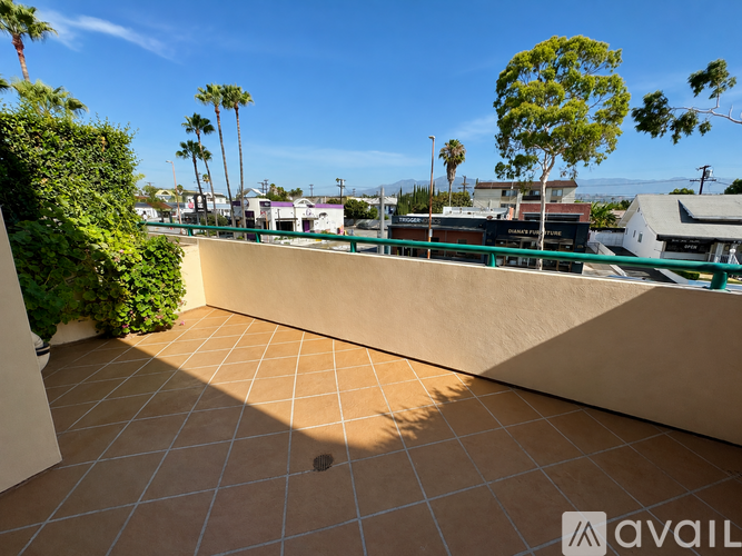 A patio with a tiled floor and a green hedge on the left.
