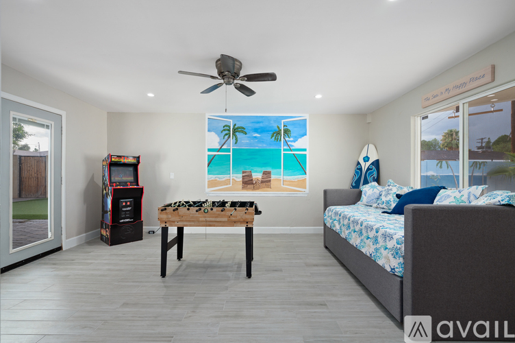 A bedroom with a bed, a table, a fridge, and a wall mural of a beach scene.