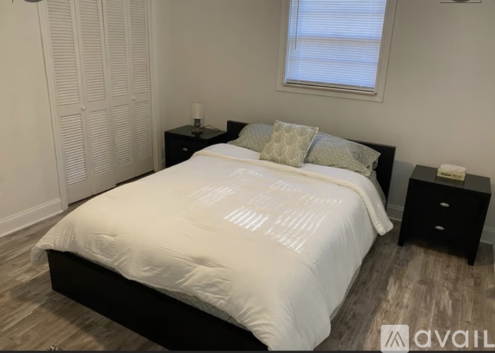 A bedroom with a bed, nightstand, and a window with blinds.