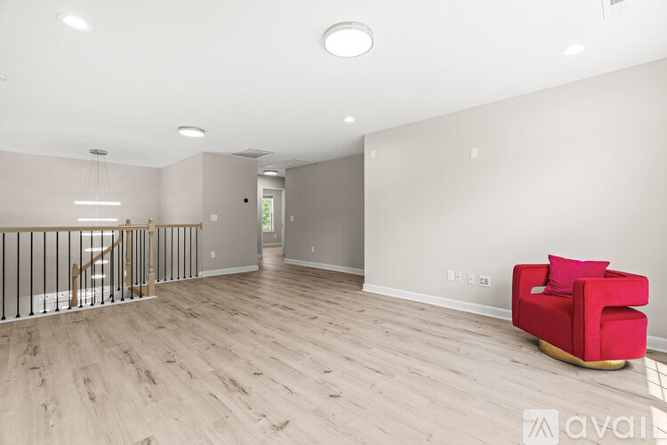 A red chair sits in a spacious room with wooden floors and white walls.