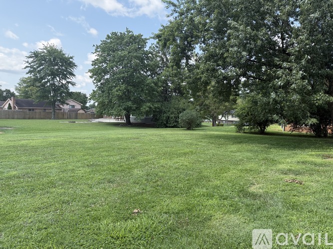 A grassy field with trees and a house in the background.