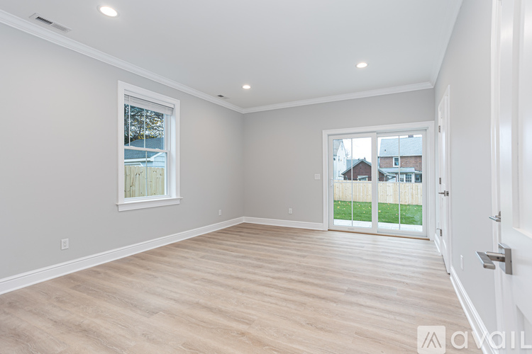 A spacious room with wooden flooring and a sliding glass door leading to a backyard.
