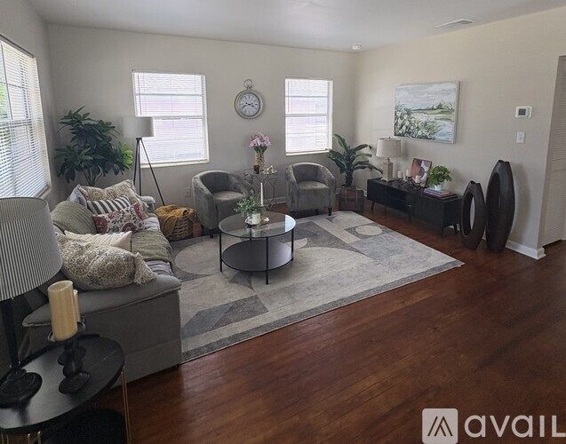 A living room with a grey sofa, a grey armchair, a grey coffee table, a grey rug, a grey side table, a grey bookshelf, a grey wall, a grey floor, a white wall, a white ce