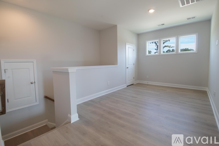 A spacious room with light wood flooring and white walls.