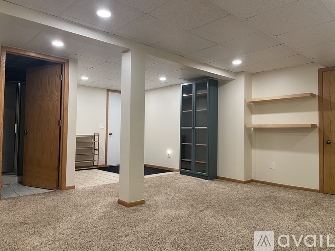 A spacious room with a carpeted floor, a wooden door, and a wall-mounted shelf.
