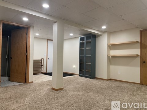 A spacious room with a carpeted floor, a wooden door, and a wall-mounted shelf.