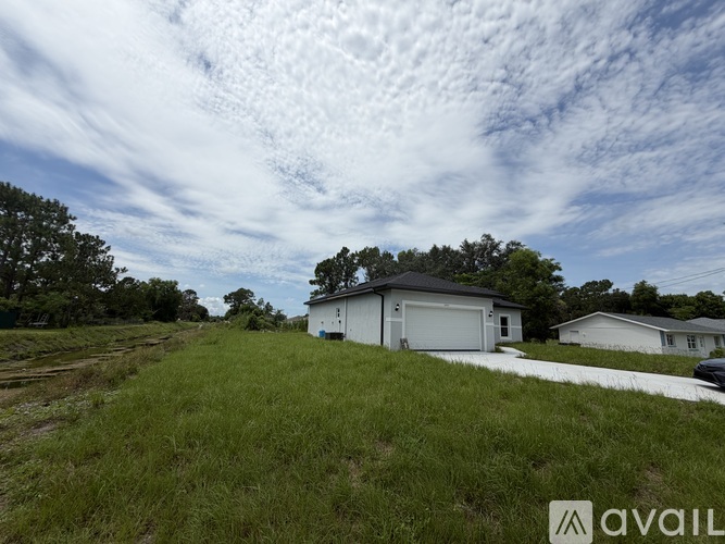 A house with a white garage door is situated in a grassy area with trees in the background.