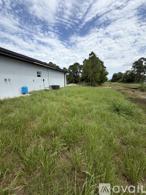 A white building with a blue barrel in front of it on a grassy field.