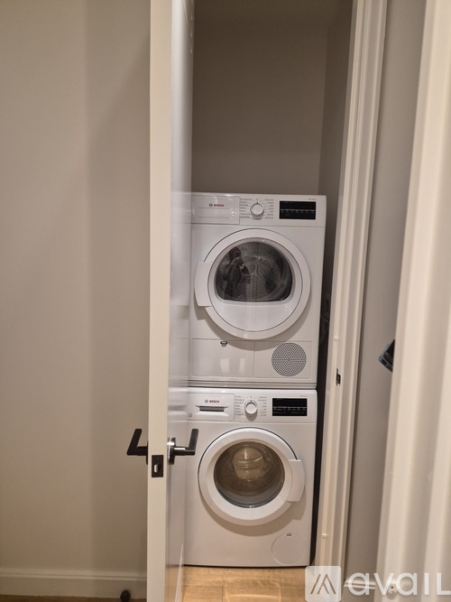 A white front load washing machine with a dryer on top is in a small room.