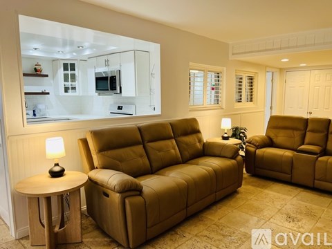 A living room with a brown leather couch and a round side table with a lamp on it.