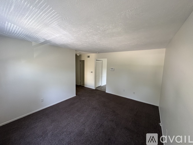 A room with carpeted floor and white walls with a doorway leading to another room.