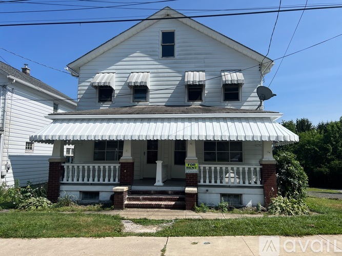 A white house with a porch and a satellite dish on the roof.