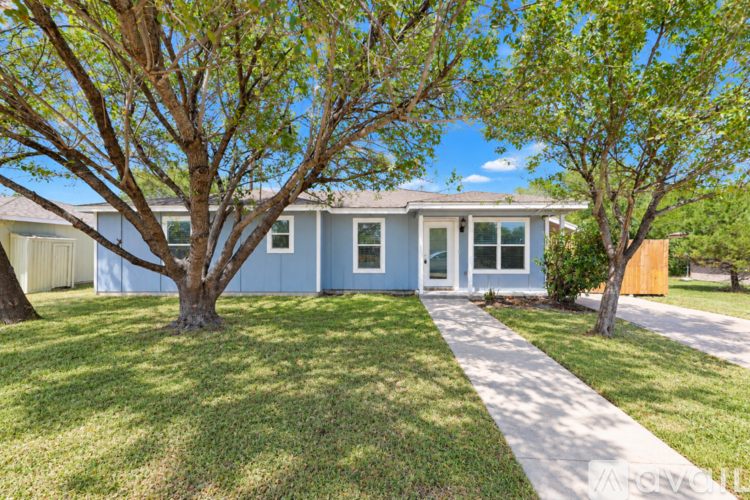 A house with a blue exterior and a white door is surrounded by green grass and trees.