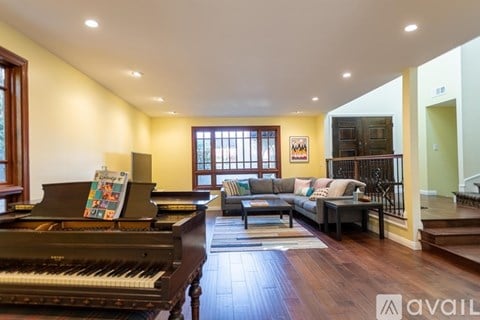 A grand piano sits in a spacious living room with a couch and a rug.