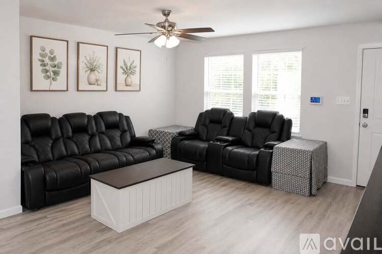 A living room with black leather furniture and a ceiling fan.
