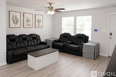 A living room with black leather furniture and a ceiling fan.
