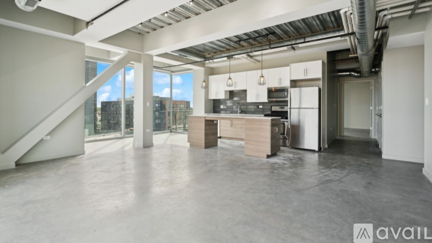 A spacious, empty room with a staircase and a kitchen area.