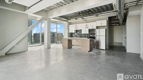 A spacious, empty room with a staircase and a kitchen area.