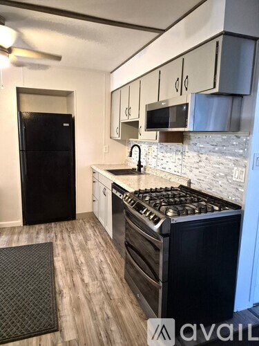 A kitchen with a black fridge, stove, and a fan on the ceiling.