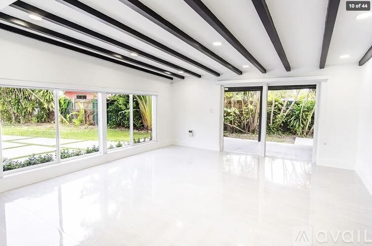 A spacious room with white walls and floor, large windows, and a ceiling with black and white stripes.